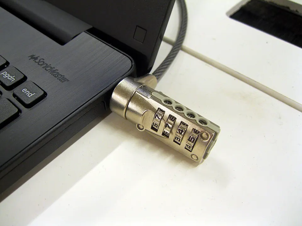 A laptop on a desk with a combination cable lock plugged into its side and looped around the desk